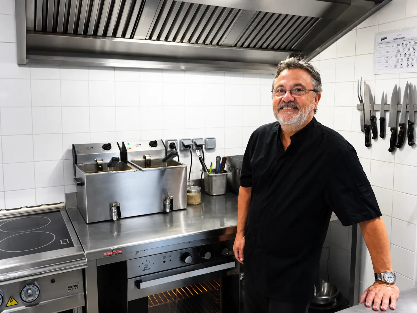 Bernard dans sa cuisine professionnelle, souriant devant son plan de travail et ses couteaux